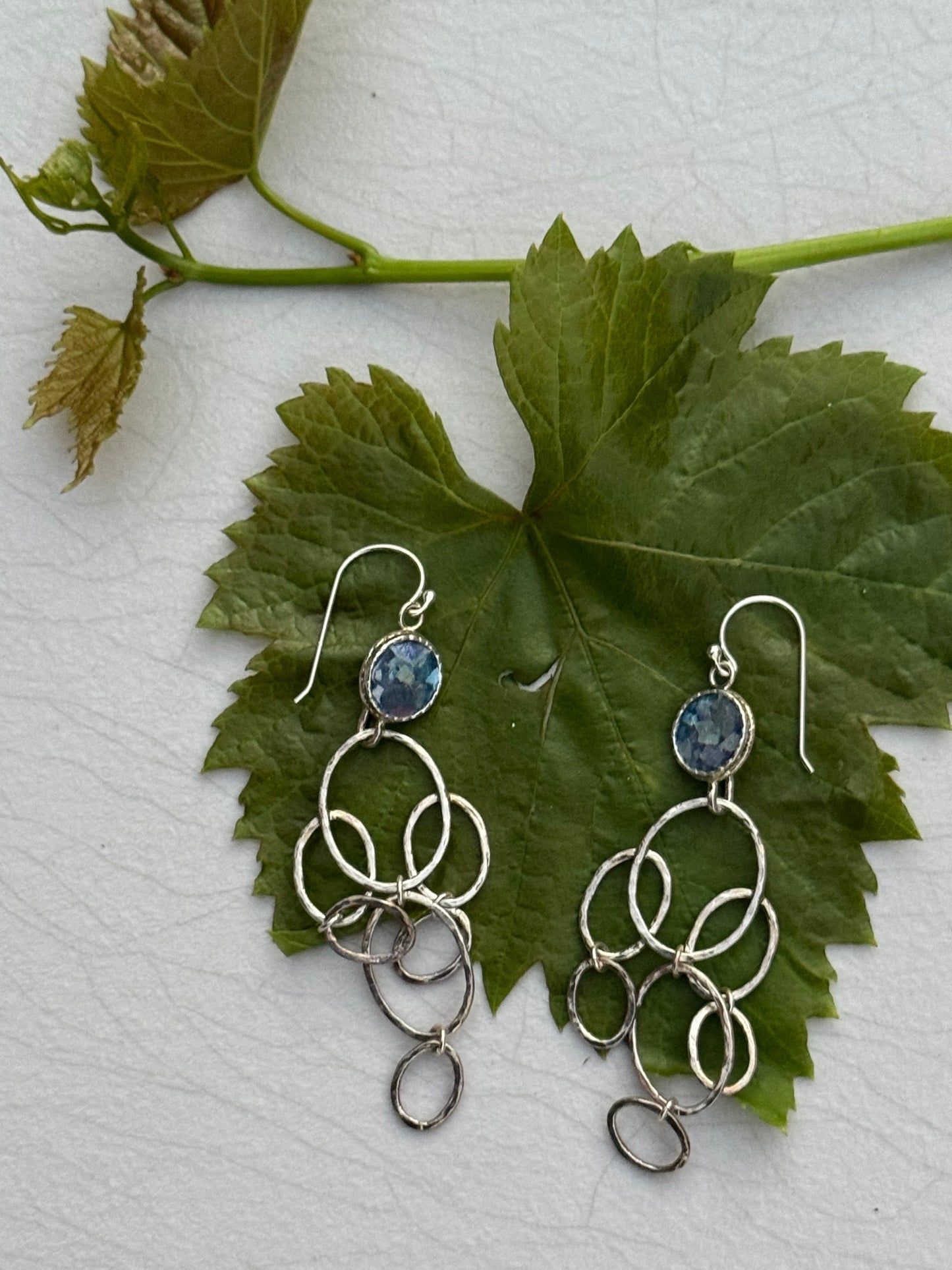 Silver dangle LONG ROMAN GLASS EARRINGS featuring multiple linked oval loops with blue gemstone accents, displayed on a green leaf background