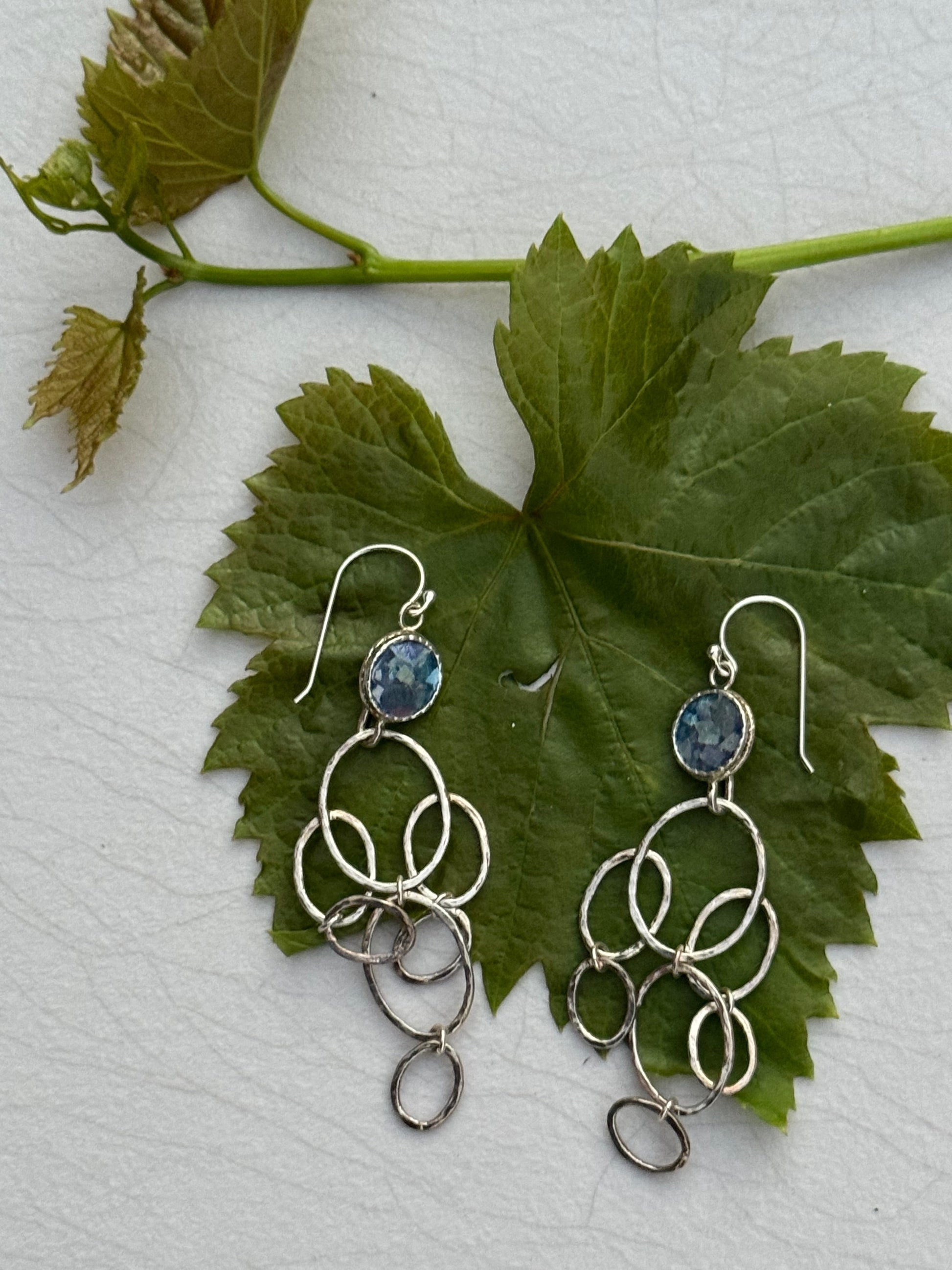 Silver dangle LONG ROMAN GLASS EARRINGS featuring multiple linked oval loops with blue gemstone accents, displayed on a green leaf background