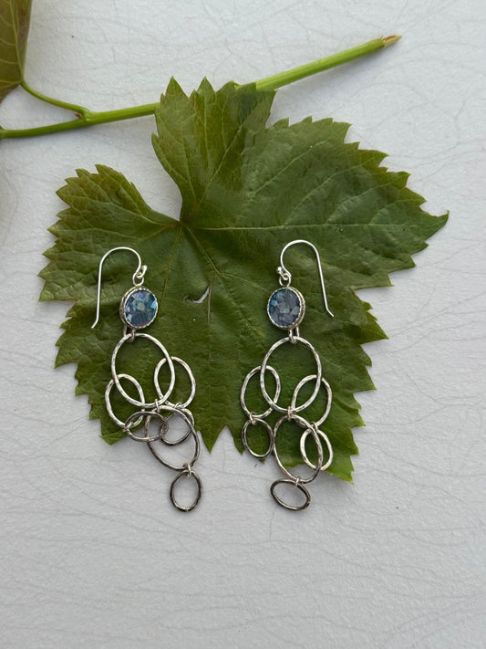 LONG ROMAN GLASS EARRINGS featuring multiple interlinked silver rings hanging below a blue Roman glass stone, displayed on a green leaf background