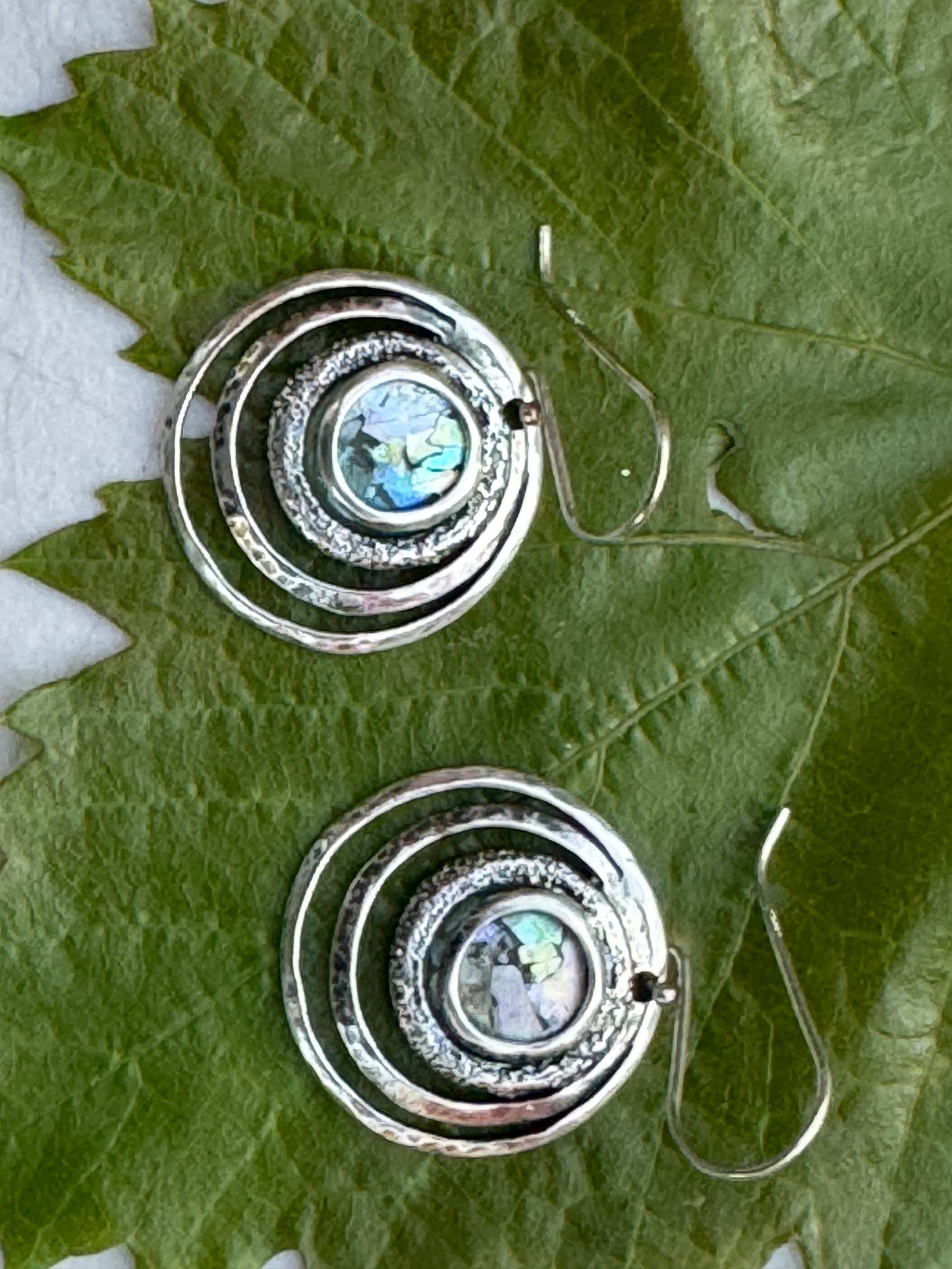 Round 3 Circles Ancient Roman Glass Sterling Earrings featuring concentric sterling silver circles with iridescent ancient Roman glass center, displayed on green leaves.