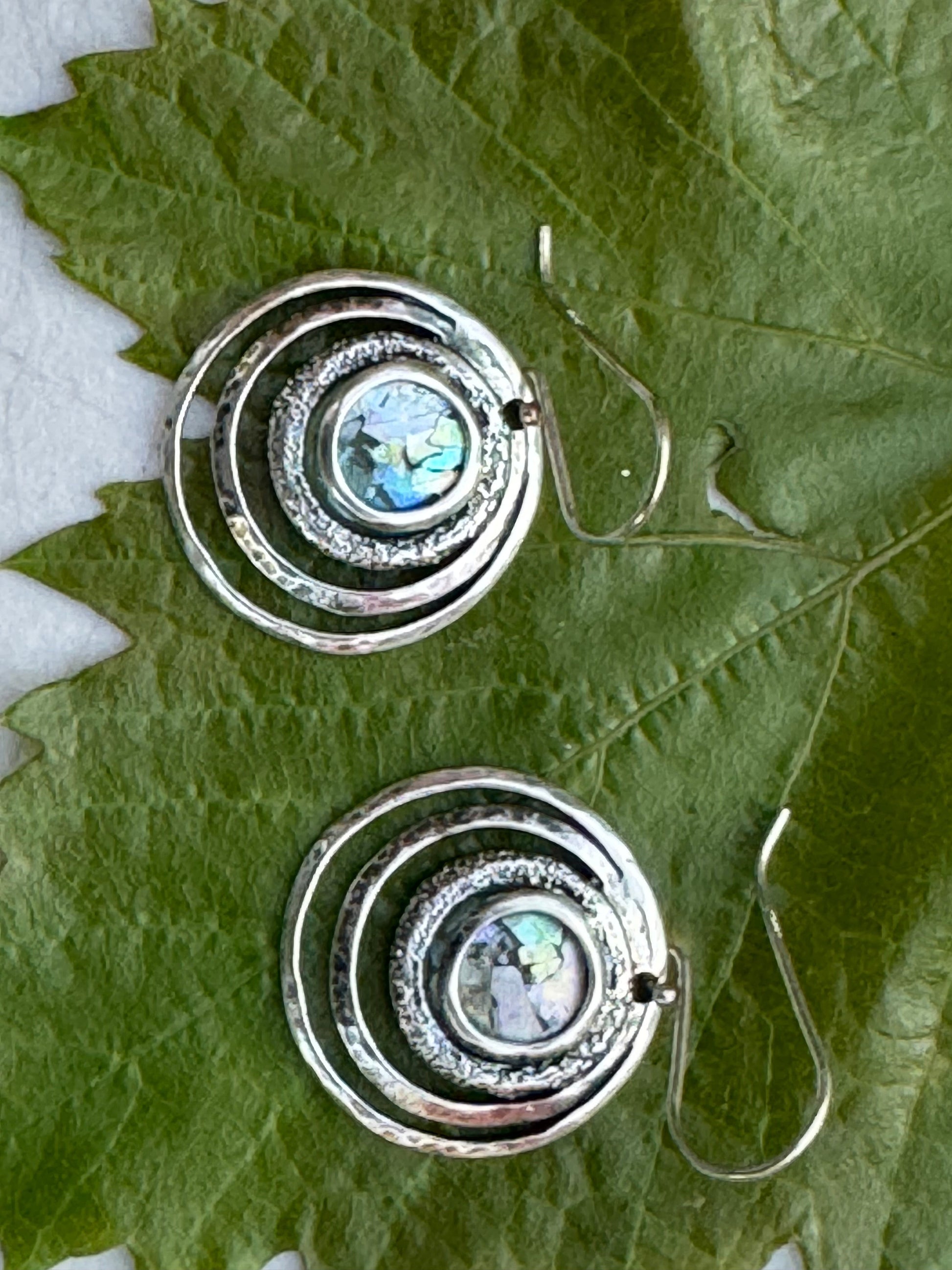 Round 3 Circles Ancient Roman Glass Sterling Earrings featuring concentric sterling silver circles with iridescent ancient Roman glass center, displayed on green leaves.
