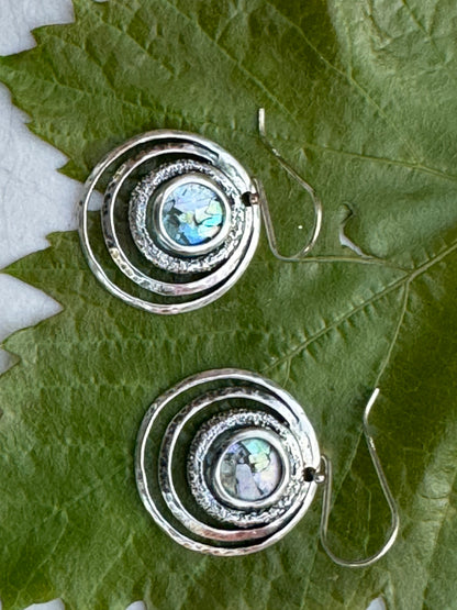 Round 3 Circles Ancient Roman Glass Sterling Earrings featuring concentric sterling silver circles with iridescent ancient Roman glass center, displayed on green leaves.