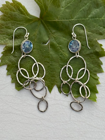 LONG ROMAN GLASS EARRINGS featuring silver interconnected loops with a blue glass stone at the top, displayed on a green leaf background.