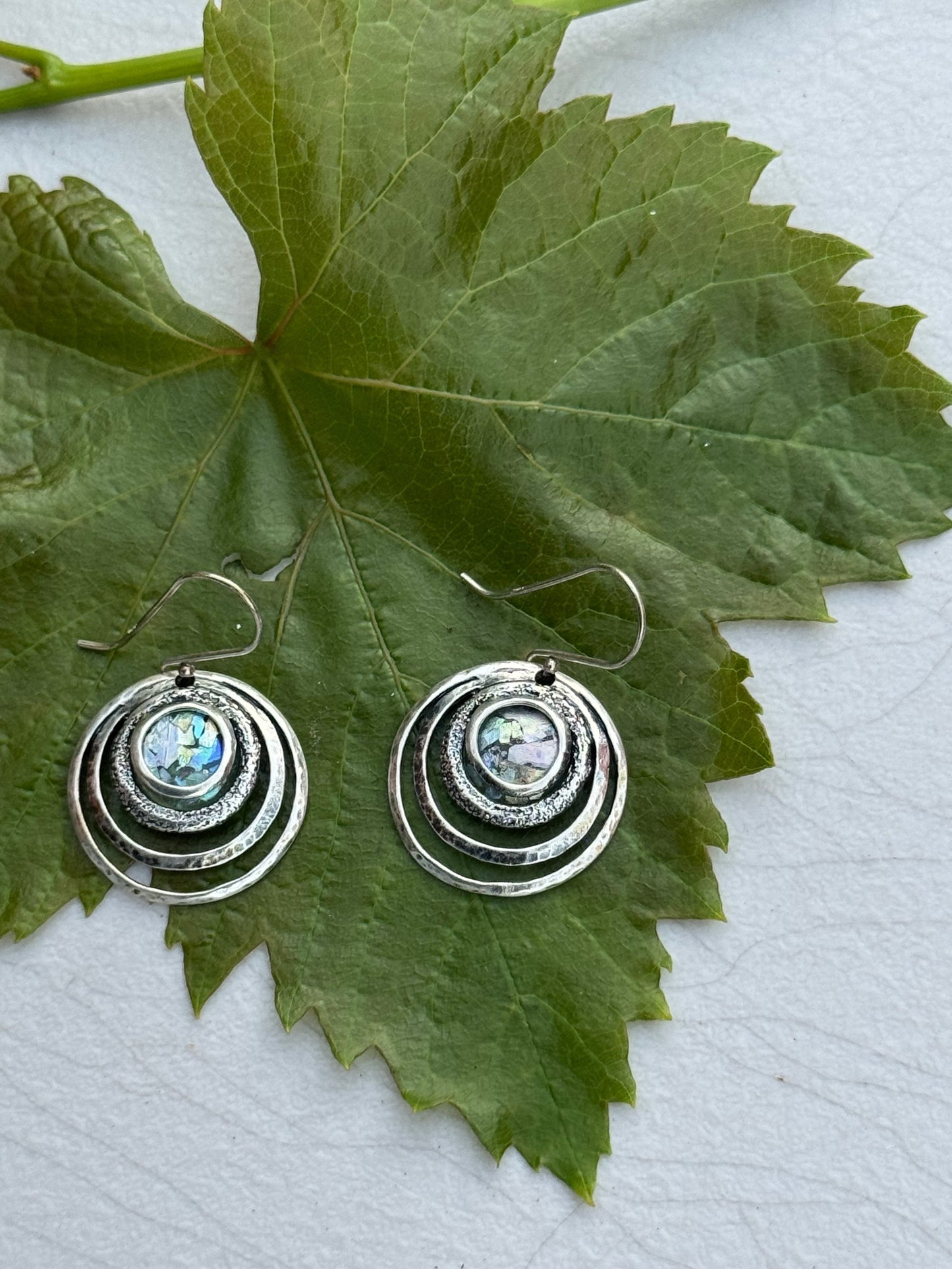Round 3 Circles Ancient Roman Glass Sterling Earrings with textured concentric circles and iridescent glass center displayed on a green leaf background