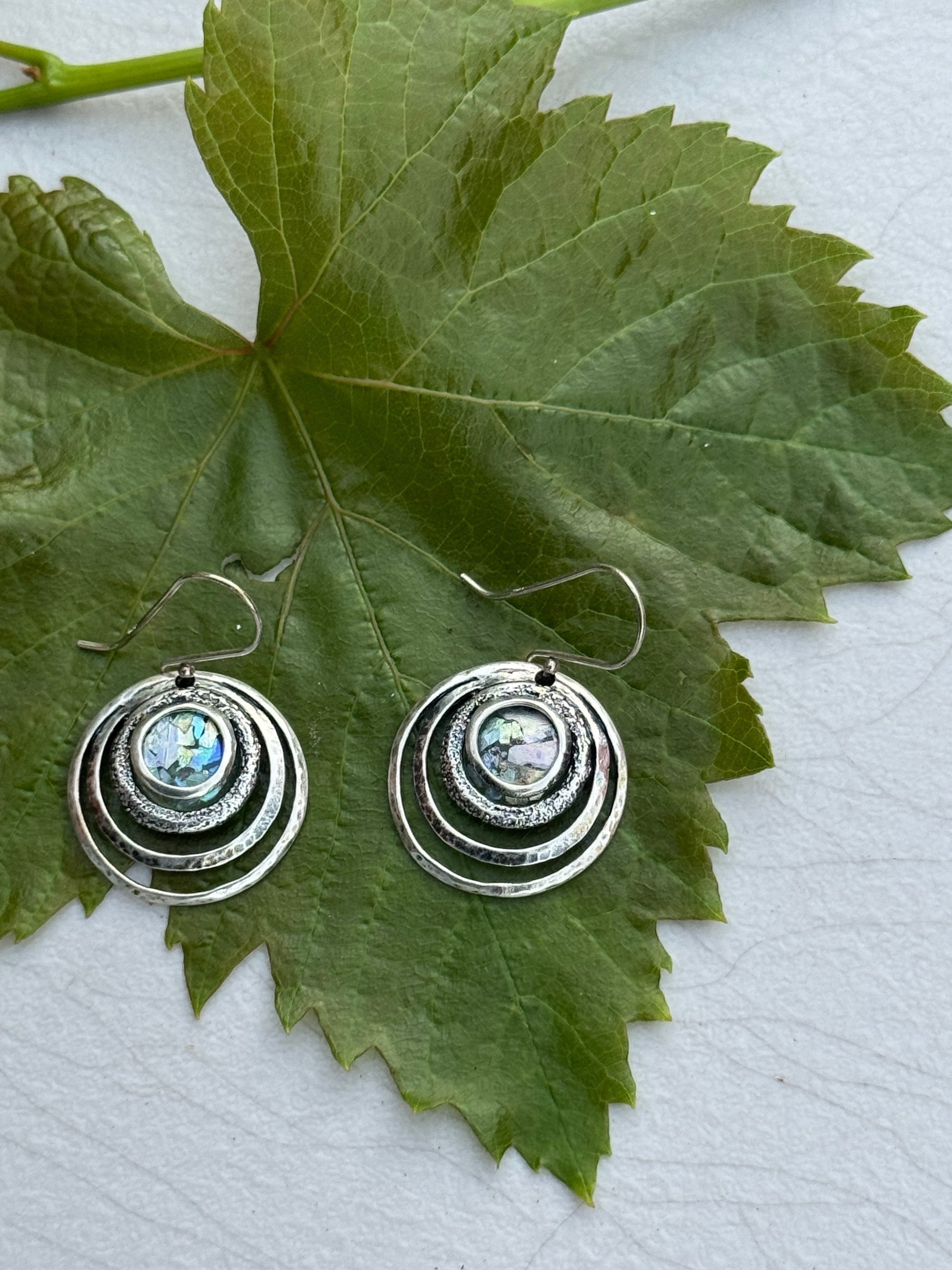 Round 3 Circles Ancient Roman Glass Sterling Earrings with textured concentric circles and iridescent glass center displayed on a green leaf background