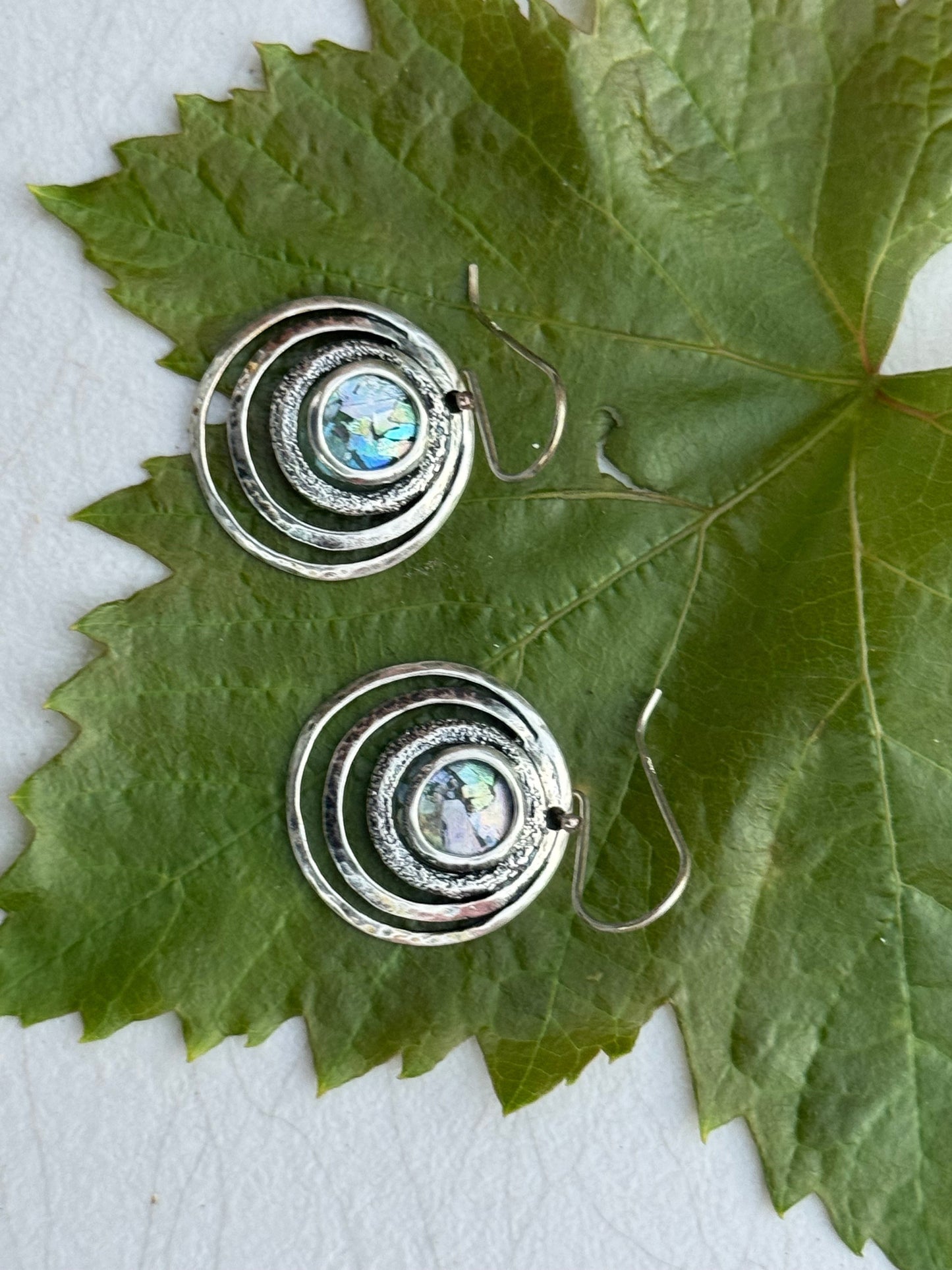 Round 3 Circles Ancient Roman Glass Sterling Earrings featuring concentric textured silver circles with iridescent ancient Roman glass centers on a green leaf background.