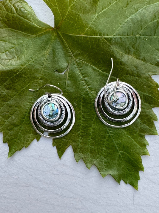 Round 3 Circles Ancient Roman Glass Sterling Earrings with concentric silver circles and iridescent ancient Roman glass centers on a green leaf background