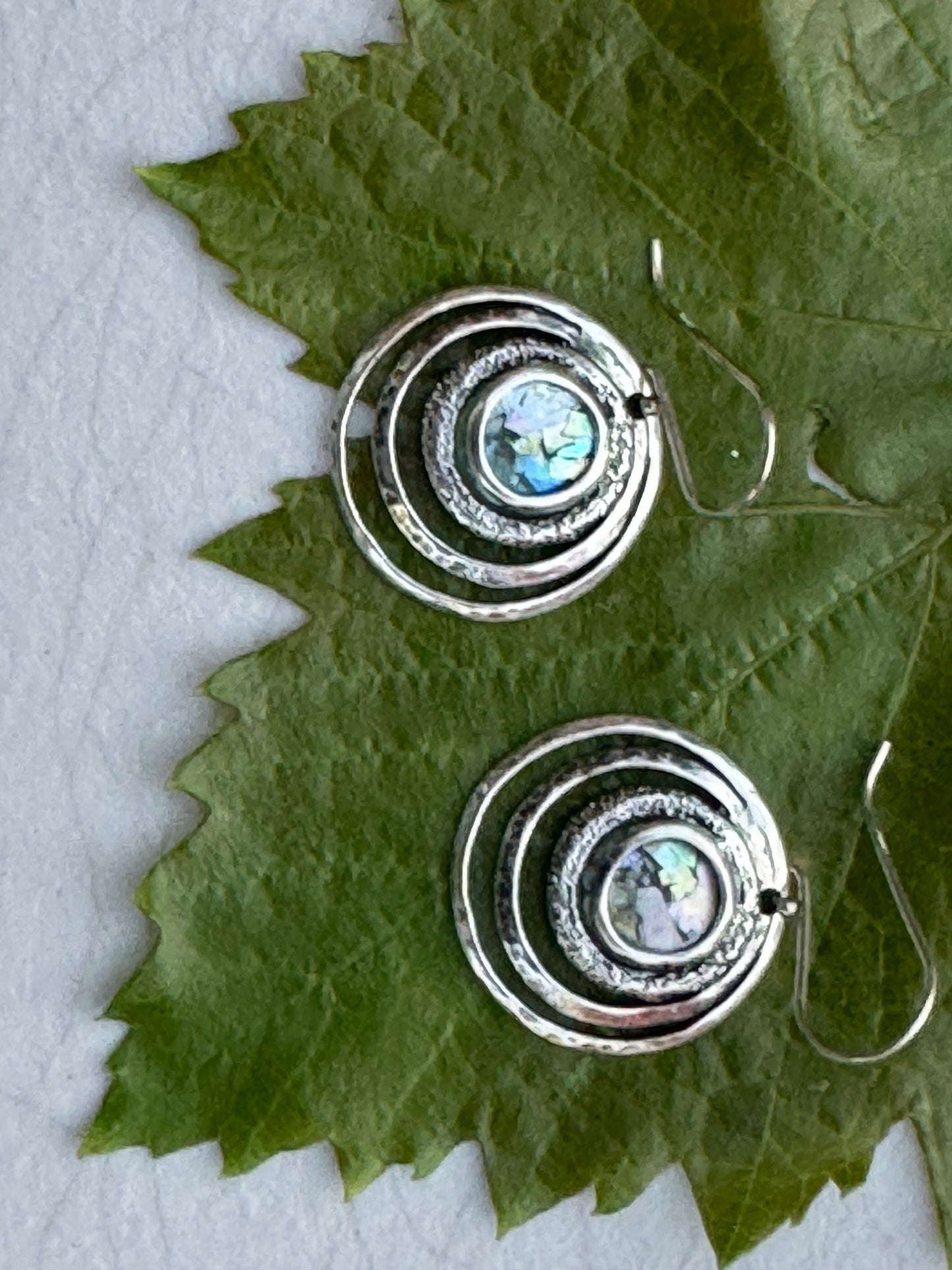 Round 3 Circles Ancient Roman Glass Sterling Earrings featuring concentric hammered silver rings with iridescent ancient Roman glass centers on green leaves background